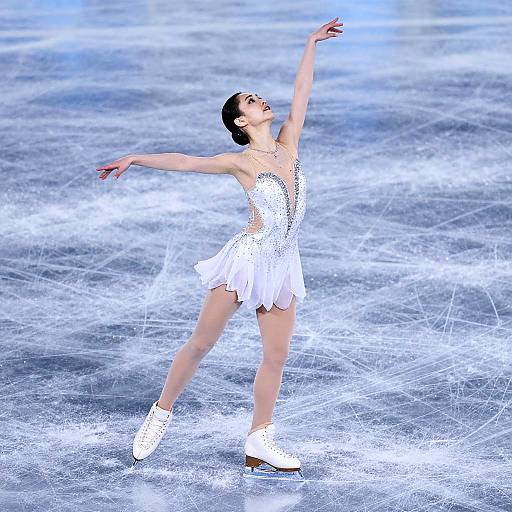 Photograph of a female ice skater in a sparkling white dress and boots, elegantly posing on a frozen rink with arms extended.