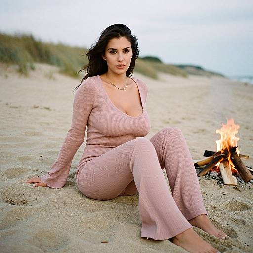 Photograph of a dark-haired woman with fair skin, wearing a pink ribbed long-sleeve and pant set, sitting on a sandy beach by