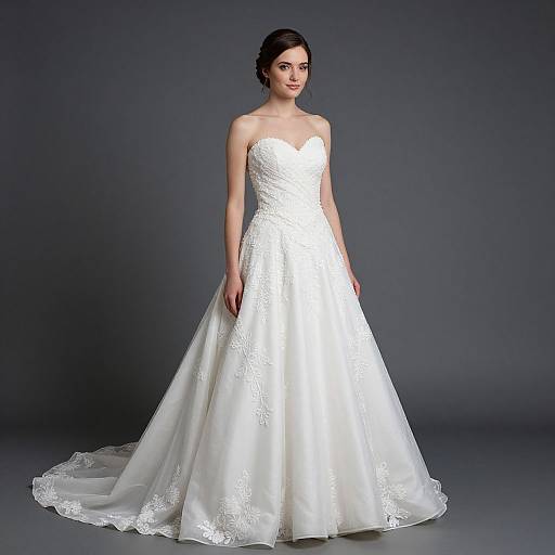 Photograph of a fair-skinned woman with dark hair in an elegant, strapless white lace wedding gown with a full skirt and long train, standing