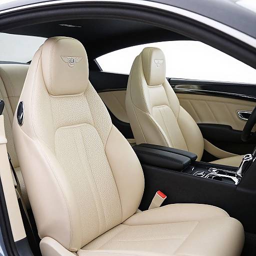 Photograph of a luxury car's interior showing two cream-colored, perforated leather seats with a Mercedes-Benz emblem, black center console, and window view