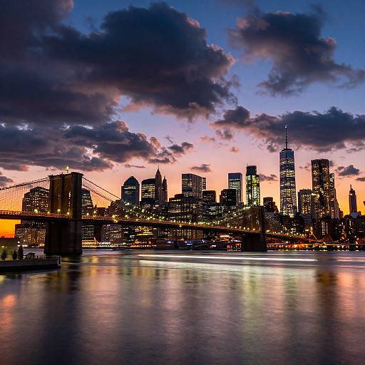 Photograph of a vibrant city skyline at dusk, featuring illuminated skyscrapers, a bridge, and colorful reflections on a calm river, under a dramatic