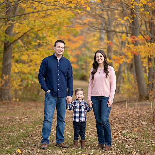 Photograph of a smiling family standing on a leafy autumn path: father in navy shirt, mother in pink sweater, son in plaid shirt,