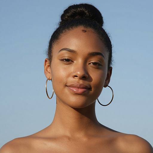 Photograph of a beautiful Black woman with smooth brown skin, dark hair in a high bun, wearing large hoop earrings, against a clear blue sky.