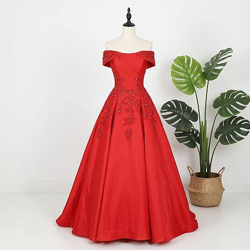 Photograph of a red, off-shoulder, ball gown with intricate embroidery, displayed on a mannequin, next to a potted mon