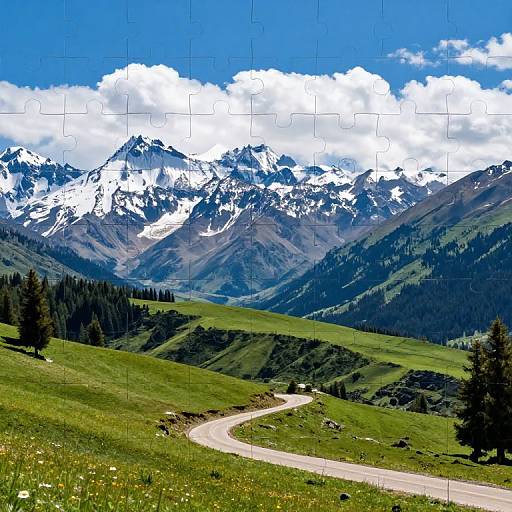 Photograph of a winding mountain road through lush green hills, leading to snow-capped peaks under a bright blue sky with white clouds.