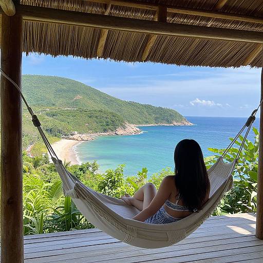 Photograph of a woman with long black hair in a blue-patterned bikini, sitting in a white hammock on a wooden deck, overlooking a vibrant