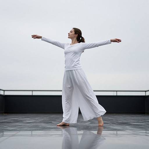 Photograph of a woman in white traditional attire, arms outstretched, barefoot, standing on a shiny black floor, against a white background.