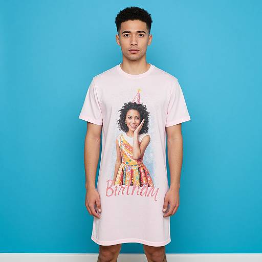 Photograph of a young Black man with short curly hair, wearing a white t-shirt with a colorful birthday graphic, standing against a bright blue background.