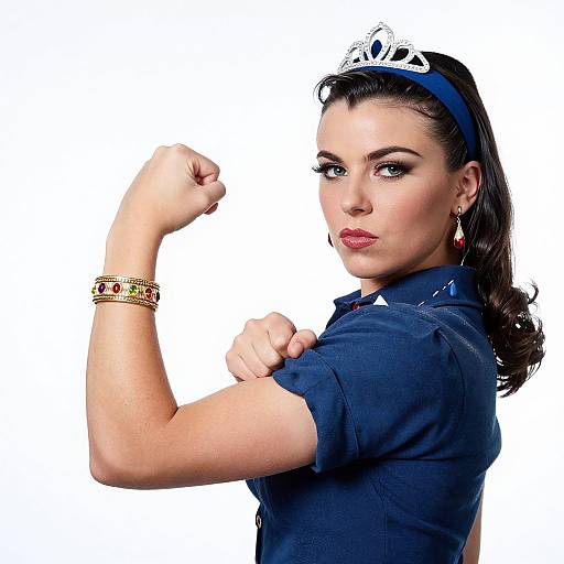 Photograph of a confident woman with dark hair, blue headband, tiara, red earrings, gold bracelets, and navy shirt, flexing her