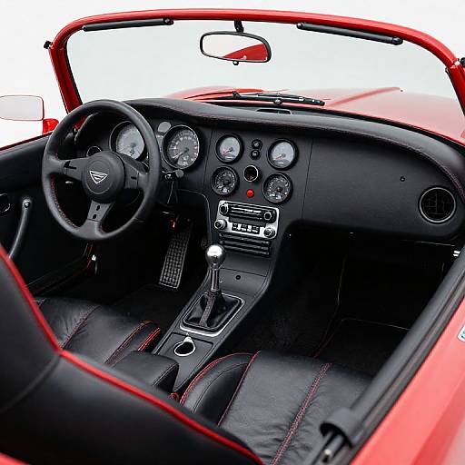 Photograph of a sleek, red sports car's interior with black leather seats, red stitching, and a classic black steering wheel with a triangular emblem.