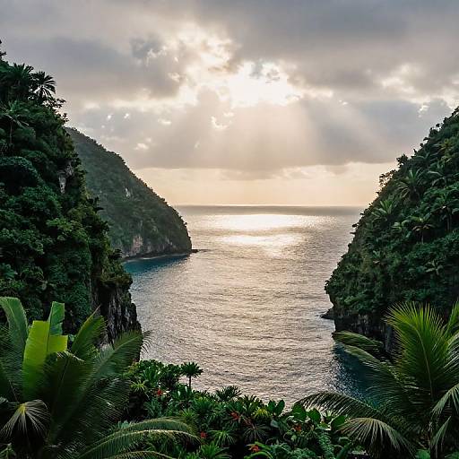 Photograph of a sunlit tropical coastline with lush green hills, dense foliage, and a shimmering blue ocean between cliffs.