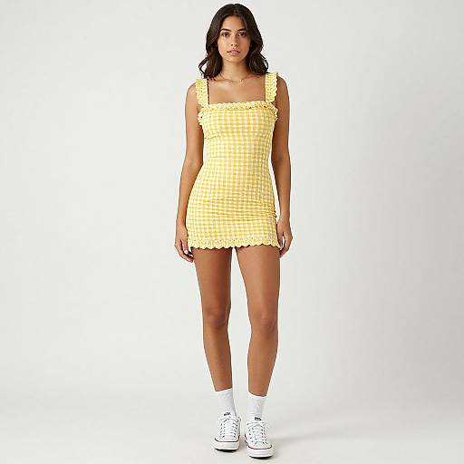 Photograph of a young woman with medium skin tone, dark wavy hair, wearing a yellow gingham sleeveless dress, white socks, and white