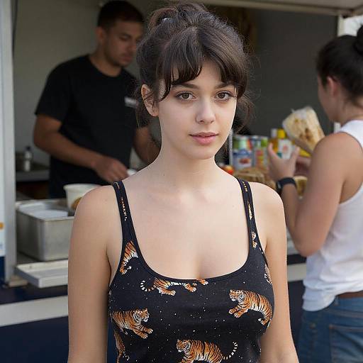 Photograph of a young woman with fair skin and dark hair in a black tank top with tiger print, standing in front of a food truck. Background