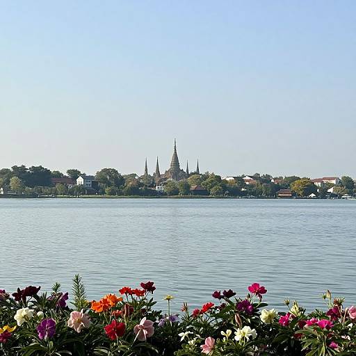 Photograph of a serene lake with vibrant flowers in the foreground, leading to a distant town featuring a prominent, tall church steeple under a clear