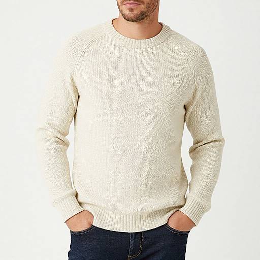 Photograph of a bearded man in a white, knitted sweater with hands in blue jeans pockets, against a plain white background.