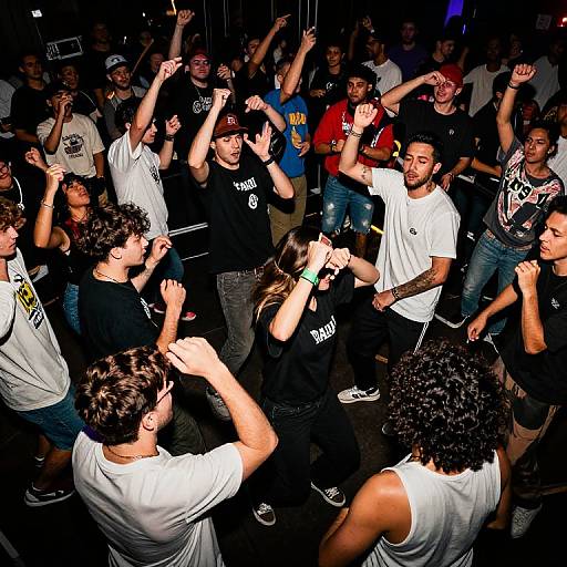 Photograph of a lively, diverse crowd of young men dancing energetically in a dimly lit club, wearing casual clothing, with arms raised and