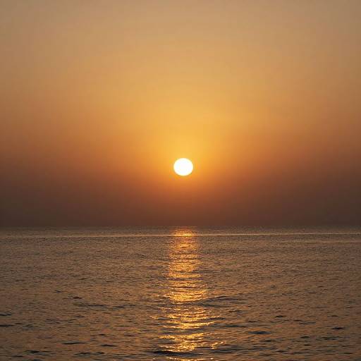 Photograph of a serene sunset over a calm ocean, with the sun glowing brightly orange, casting a golden reflection on the water.