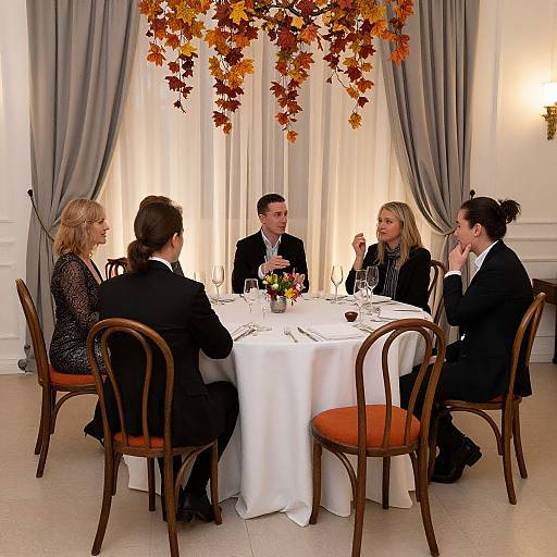 Photograph of six formally dressed people, three men and three women, seated around a white-clothed table with autumn leaf decor, in an elegant
