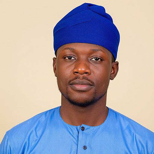 Photograph of a serious-looking Black man with dark skin, wearing a blue knitted cap and matching blue button-up shirt, against a plain white background