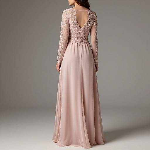 Photograph of a woman in a floor-length, pink, lace-backed gown with long sleeves, standing against a plain, gray background.