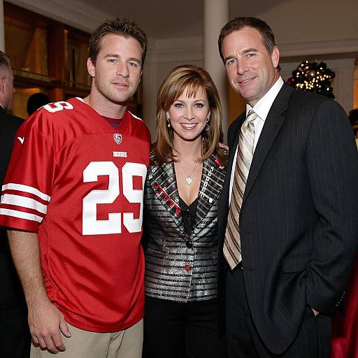 Photograph of three people: a man in a red football jersey with number 29, a woman in a patterned blazer, and another man