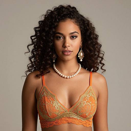 Photograph of a beautiful young woman with curly black hair, wearing an orange lace bralette, pearl necklace, and dangling earrings, against a plain gray