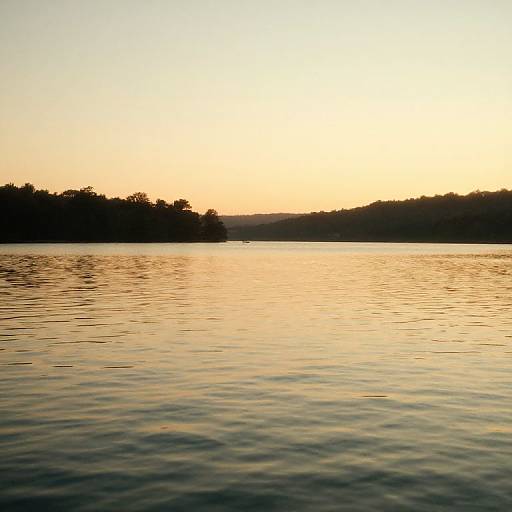Photograph of a serene lake at sunset, with a golden sky, calm water, and dark silhouetted tree line in the background.