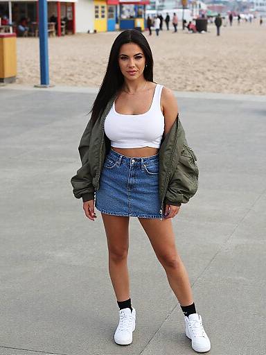 Photograph of a young woman with long black hair, tan skin, and medium build, wearing a white crop top, green jacket, blue denim skirt