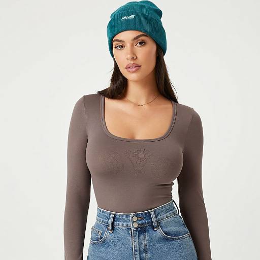 Photograph of a young woman with long black hair, wearing a teal beanie, grey long-sleeve top, and high-waisted blue