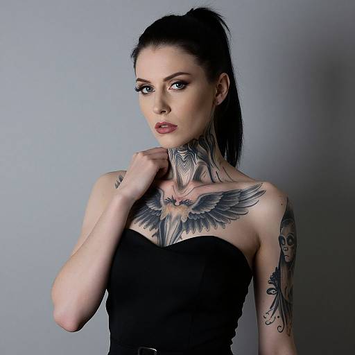 Photograph of a pale-skinned woman with black hair in a ponytail, wearing a strapless black top, showcasing extensive neck and chest tattoos,