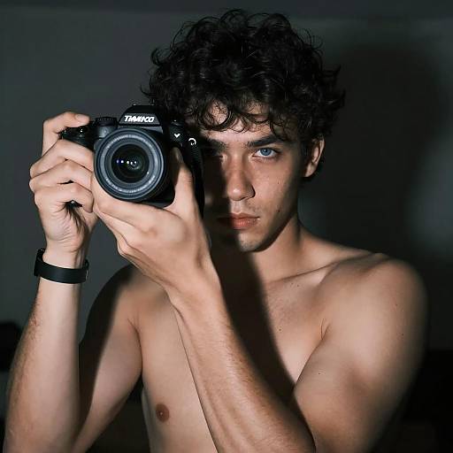 Shirtless Man Holding Camera in Dark Room