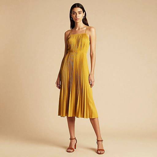 Photograph of a slender woman with long dark hair, wearing a yellow pleated dress and red sandals, standing against a plain beige background.