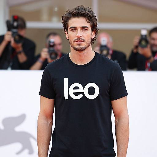 Photograph of a handsome, dark-haired man with light skin, wearing a black t-shirt with the white 