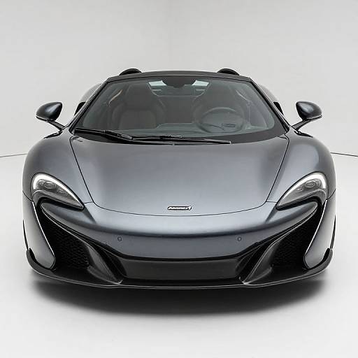 Photograph of a sleek, black, modern sports car with glowing headlights, viewed from the front, set against a white background.