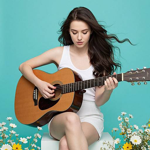 Photograph of a fair-skinned woman with long black hair, wearing a white dress, playing an acoustic guitar against a turquoise background with white and yellow