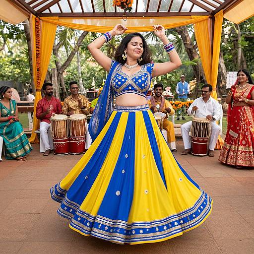 Photograph of a dancing woman in a vibrant blue and yellow traditional Indian outfit, surrounded by musicians and spectators under a canopy.