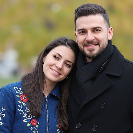 Photograph of a smiling couple with dark hair; woman in blue embroidered coat, man in black coat, standing close outdoors.