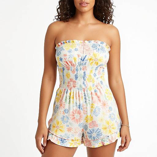 Photograph of a woman with curly hair, wearing a strapless, white floral romper with yellow and blue patterns, standing against a plain white background