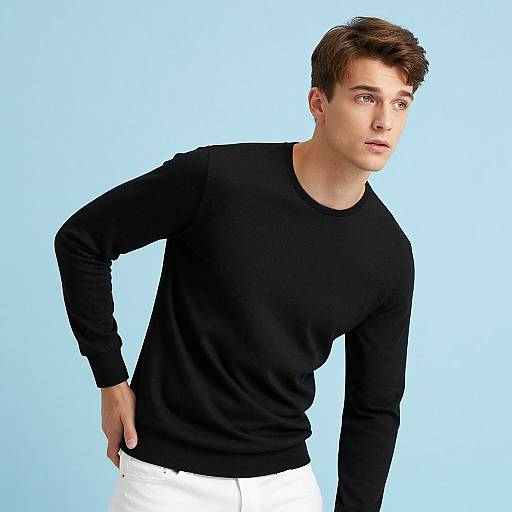 Photograph of a young man with short brown hair, wearing a black long-sleeve shirt and white pants, leaning slightly forward against a light blue