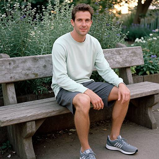 Photograph of a fit, light-skinned man with short brown hair, wearing a white sweatshirt, gray shorts, and gray sneakers, sitting on