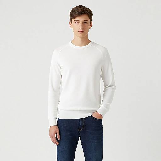 Photograph of a young man with short brown hair, wearing a plain white long-sleeve shirt and dark blue jeans, standing against a plain white