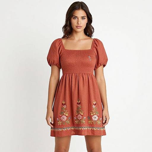 Photograph of a young woman with wavy dark hair wearing a short-sleeved, red floral-embroidered dress against a white background.