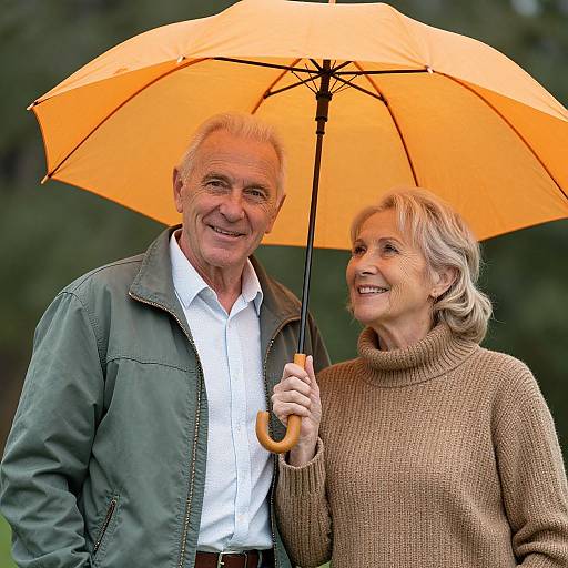 Photograph of an elderly white couple smiling under an orange umbrella, the man in a green jacket and white shirt, the woman in a brown turt