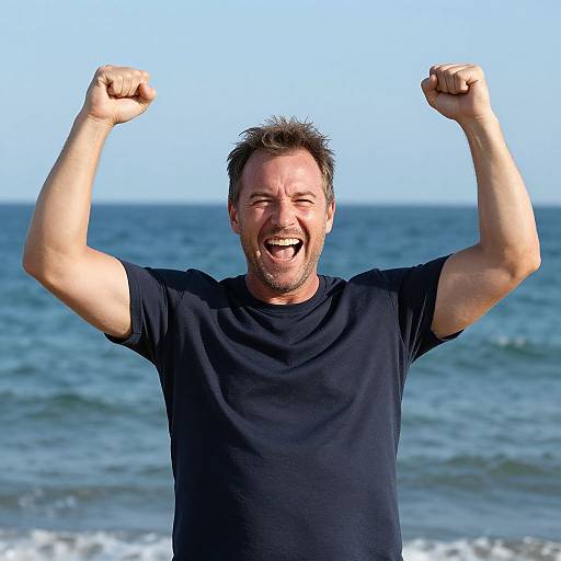 Photograph of a smiling, middle-aged man with short brown hair, raising both fists in triumph against a clear blue ocean backdrop. He wears a black