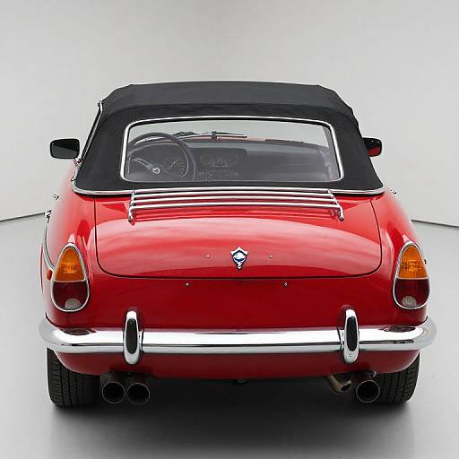 Photograph of a shiny red classic convertible car viewed from the rear, with black soft top, chrome bumper, dual exhausts, and orange tail lights
