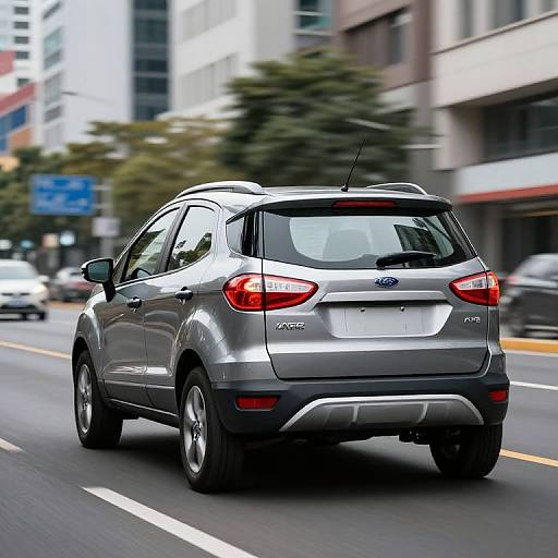 Photograph of a silver Ford Edge SUV driving on a city street, with blurred buildings and cars in the background.