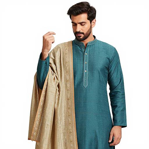 Photograph of a bearded man with dark hair, wearing a teal traditional long kurta and gold embroidered shawl, looking down, white background.