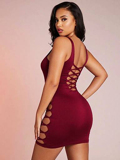Photograph of a curvy, light-skinned woman with black hair, wearing a tight, maroon mini dress with cut-out sides, standing against
