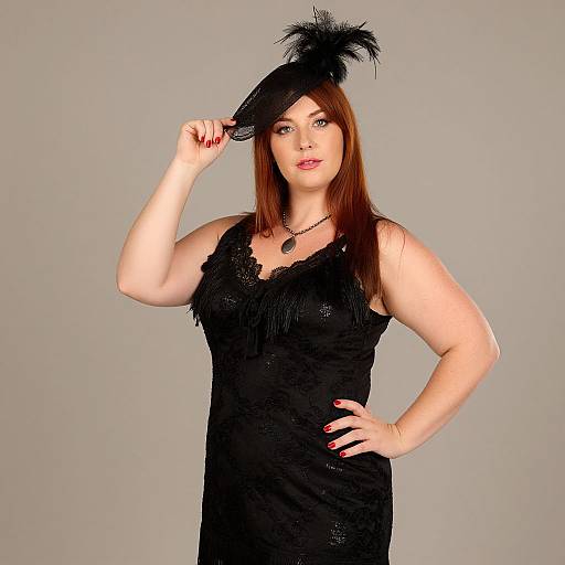 Photograph of a fair-skinned woman with straight red hair, wearing a black fringe dress and feathered hat, posing against a gray background, hand