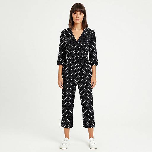 Photograph of a young woman with straight brown hair, wearing a black polka dot jumpsuit, V-neck, 3/4 sleeves, and